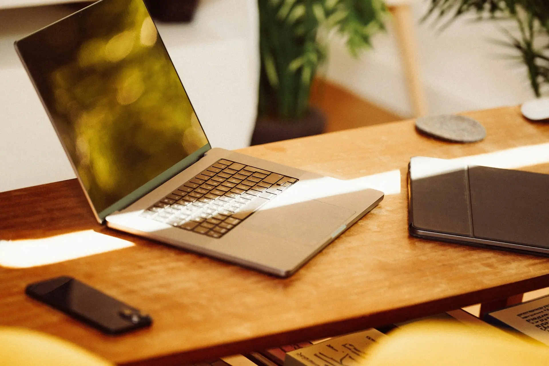 Laptop and smartphone on a wooden desk with sunlight streaming in.